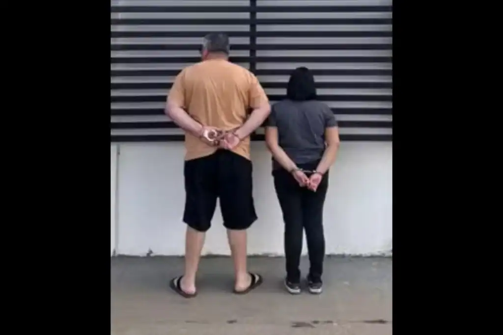 Imagem de costas do casal suspeito de estelionato sendo preso pela polícia.