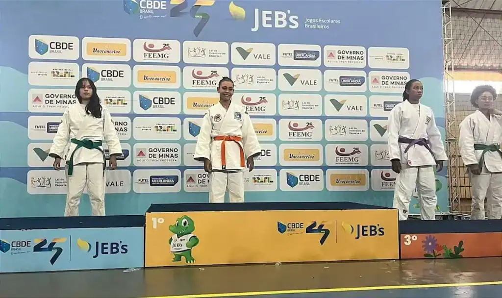 Atleta Lívia Pacheco, vestindo quimono de judô, celebrando vitória no pódio.