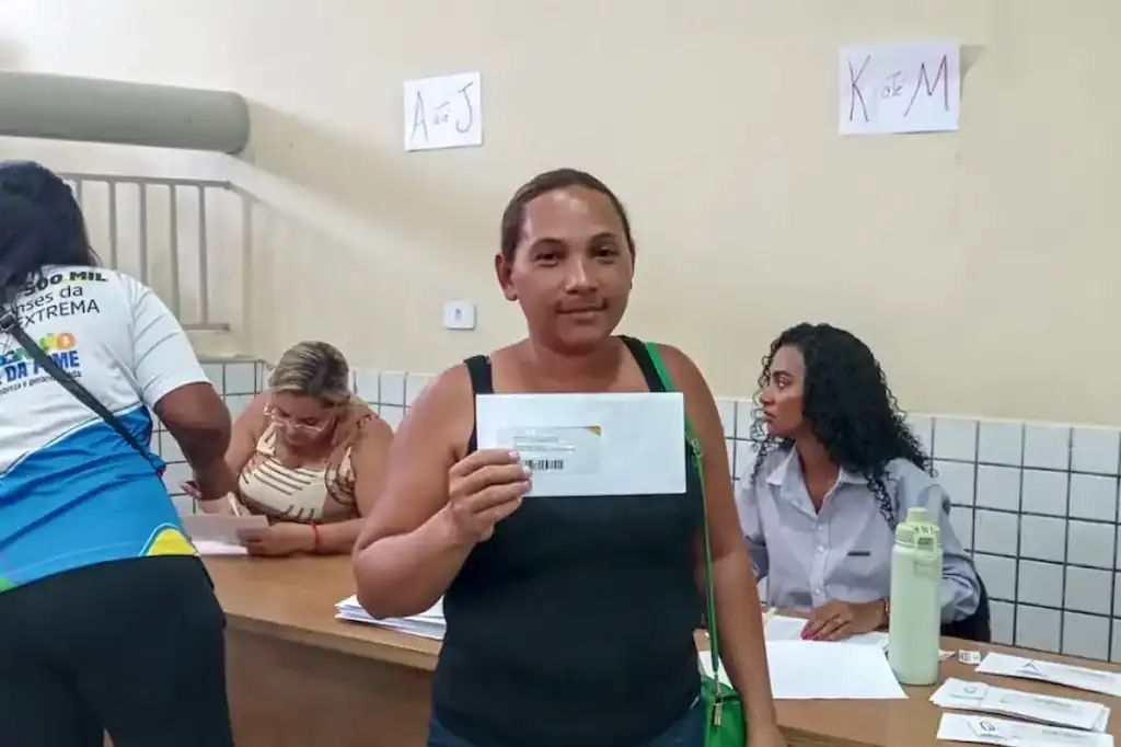 Beneficiária sorridente segurando o cartão do programa social na mão